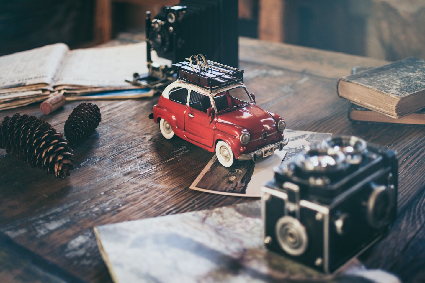 Voiture rouge vintage sur une carte, entourée d'appareils photo et de livres anciens.