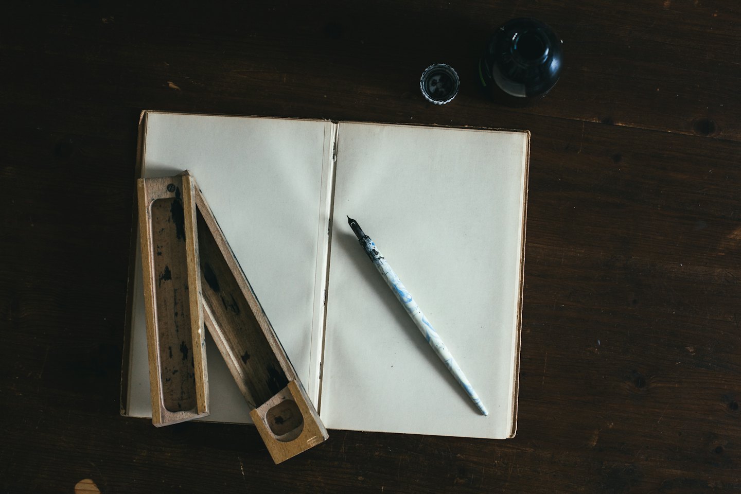 Cahier vierge et outils d'écriture anciens sur une table en bois.