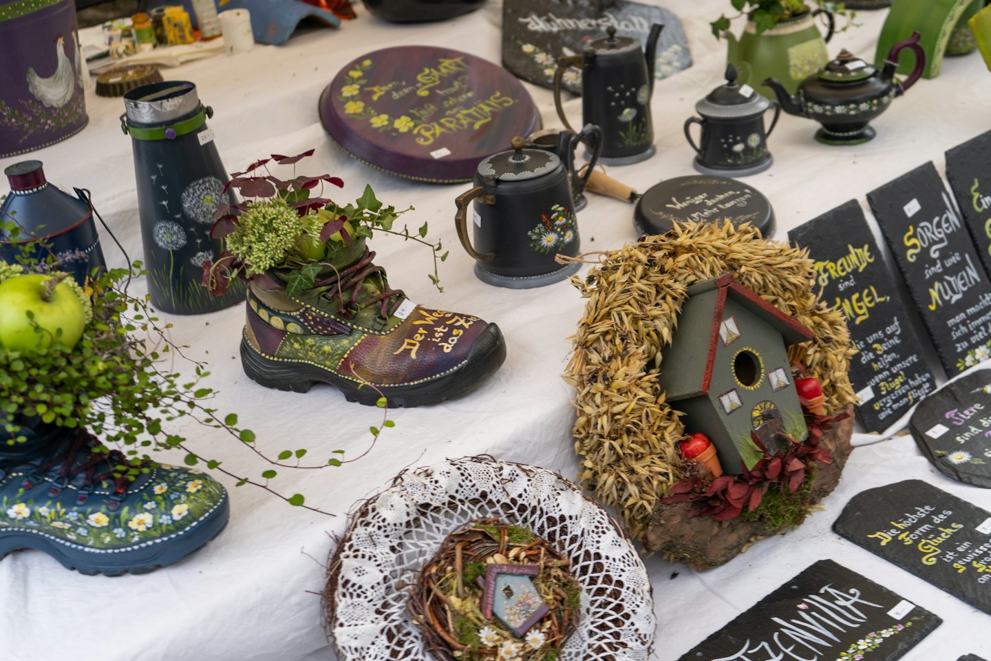 Artisanat fait main, dont des jardinières peintes en forme de bottes et des plaques en ardoise exposées.