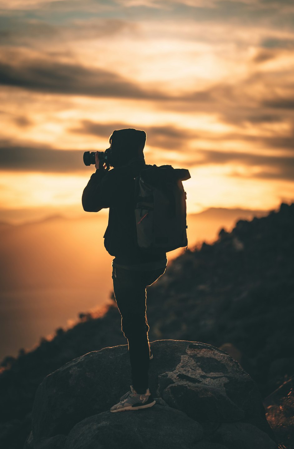 Photographe en contre-jour devant un coucher de soleil éclatant sur les montagnes.