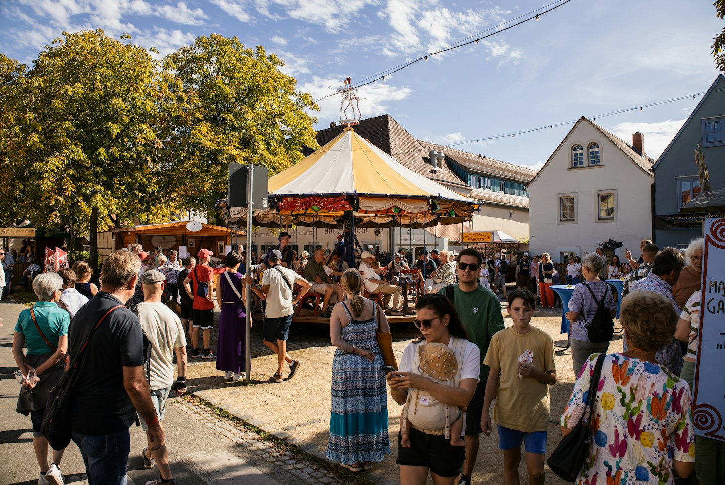 Des gens explorent un marché extérieur avec un carrousel et des bâtiments historiques.
